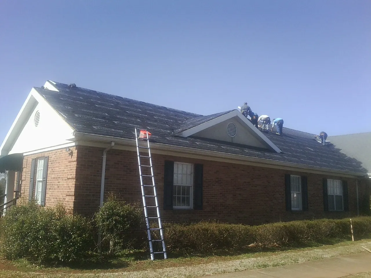 Crew tearing shingles off a brick ranch roof with a ladder set — Metal Roof Repair work by our crew in Drain
