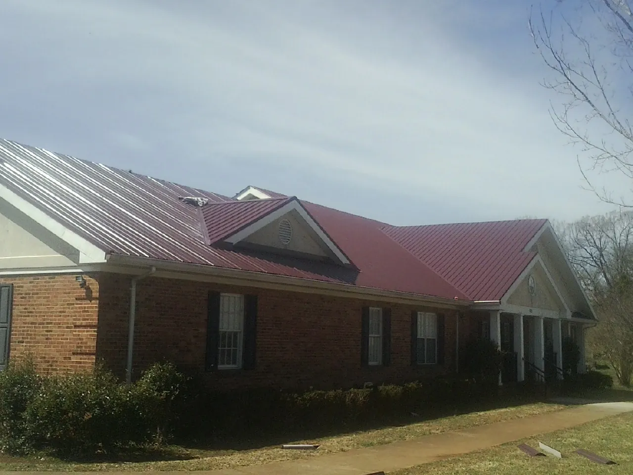 Red metal roof with gabled entries on a long brick building, from a Hail Damage Roof Repair job in Drain