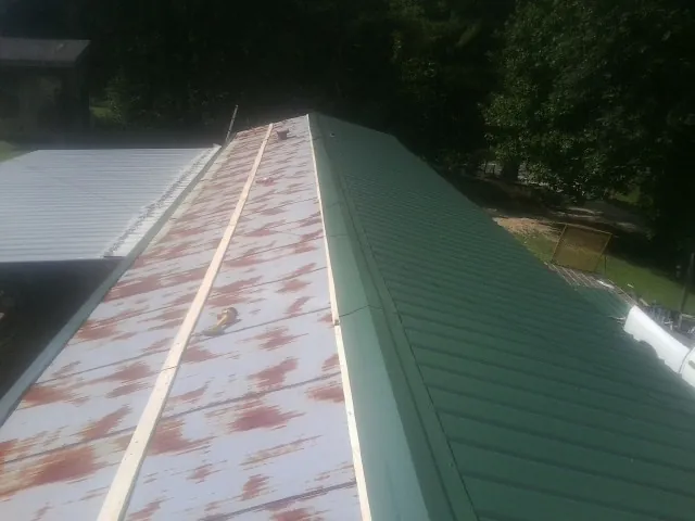 Old rusted panels beside newly installed green metal roofing — Wind Damage Roof Repair by Roofing Brothers in Drain